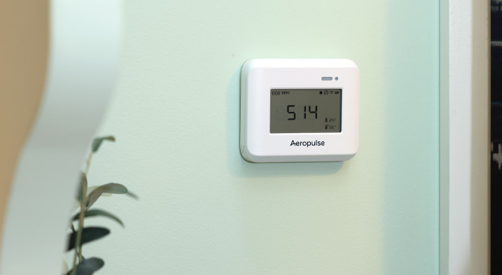 Wall-mounted Aeropulse A100 indoor air quality sensor in a commercial workspace with positive customer feedback on accuracy and performance.